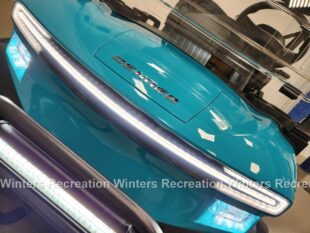 A close-up of a bright turquoise vehicle's front, featuring sleek headlights and a modern design.